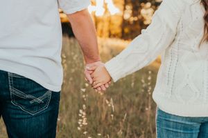 Couple holding hands in casual attire against sunset backdrop.