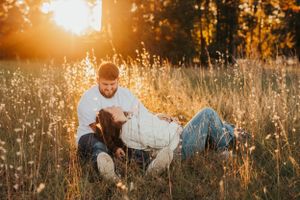 Couple relaxing in tall grass field during golden hour sunset.
