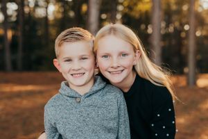 Siblings smiling together in an autumn forest setting.