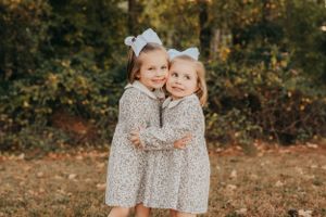 Sisters in matching dresses share a sweet moment together outdoors.