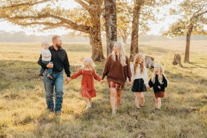 Large family walking together through a sunlit field with tall trees during golden hour.