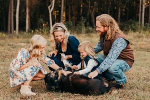 A family plays with their dog in a grassy field during an outdoor photo session.