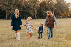 A family walks hand in hand through a golden grass field at sunset.