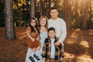 Family of four poses together in a wooded area during sunset.