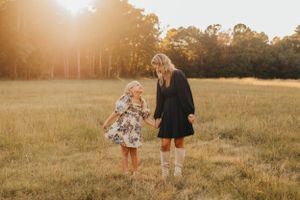 Mother and daughter walk together in a sun-drenched field during golden hour.