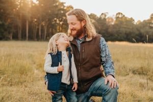 Father and son share a candid laughing moment in a sunlit field.