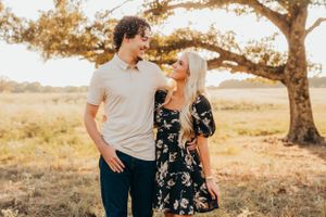 Couple standing together in casual attire against sunset backdrop with autumn tree.