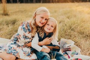 Big sister and little brother sitting on a blanket in a golden field with a dog.
