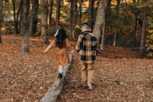 Two children walking together on a fallen tree trunk in an autumn forest.