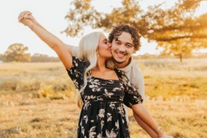Couple in casual wear embracing playfully in golden sunset field.
