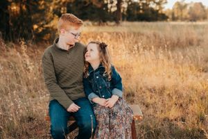 Siblings sitting together in tall grass during golden hour.