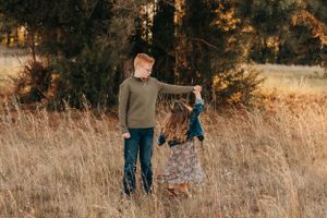 Siblings playing in a field of tall grass at sunset.