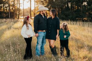 Family of four standing together in a sunlit meadow at golden hour.