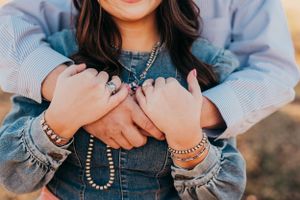 Close-up of embracing hands wearing bracelets and denim clothing in warm sunlight.