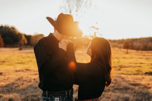 Silhouetted couple embracing in a field during golden hour with sun flare.