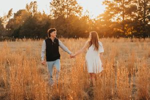 Couple holding hands while walking through tall golden grass at sunset.