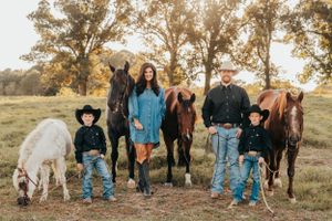Family poses with horses in an autumn field at sunset.