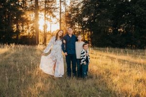 Family portrait in a golden meadow with sunset filtering through pine trees.