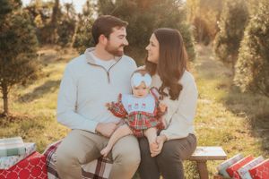 Family shares tender moment on blanket with Christmas presents and decorations in outdoor setting.