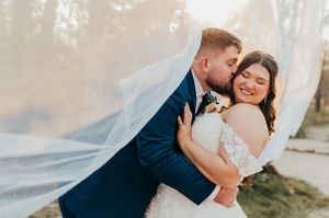 A couple shares an intimate moment under flowing white veil during their outdoor wedding photoshoot.