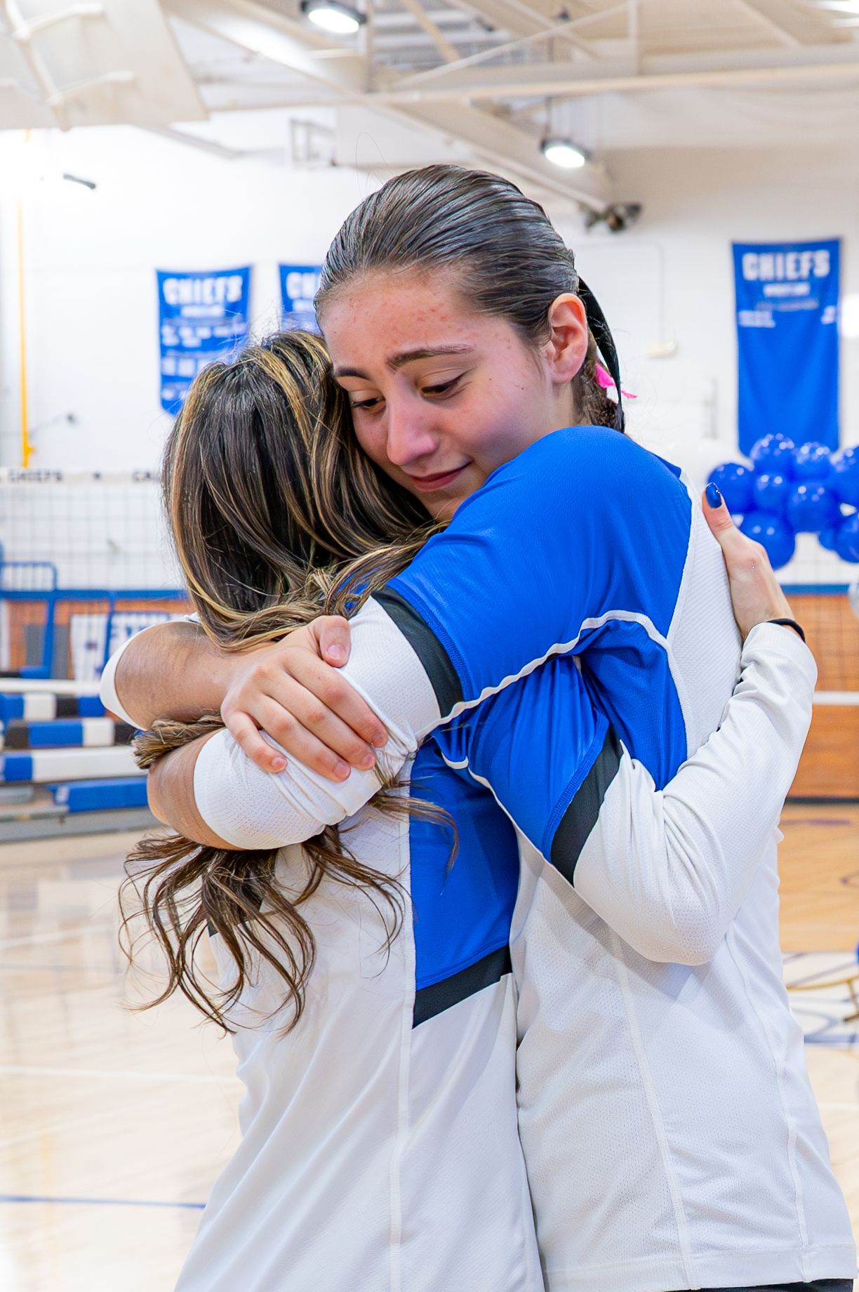 Athletes in blue and white uniforms sharing emotional embrace in gymnasium.