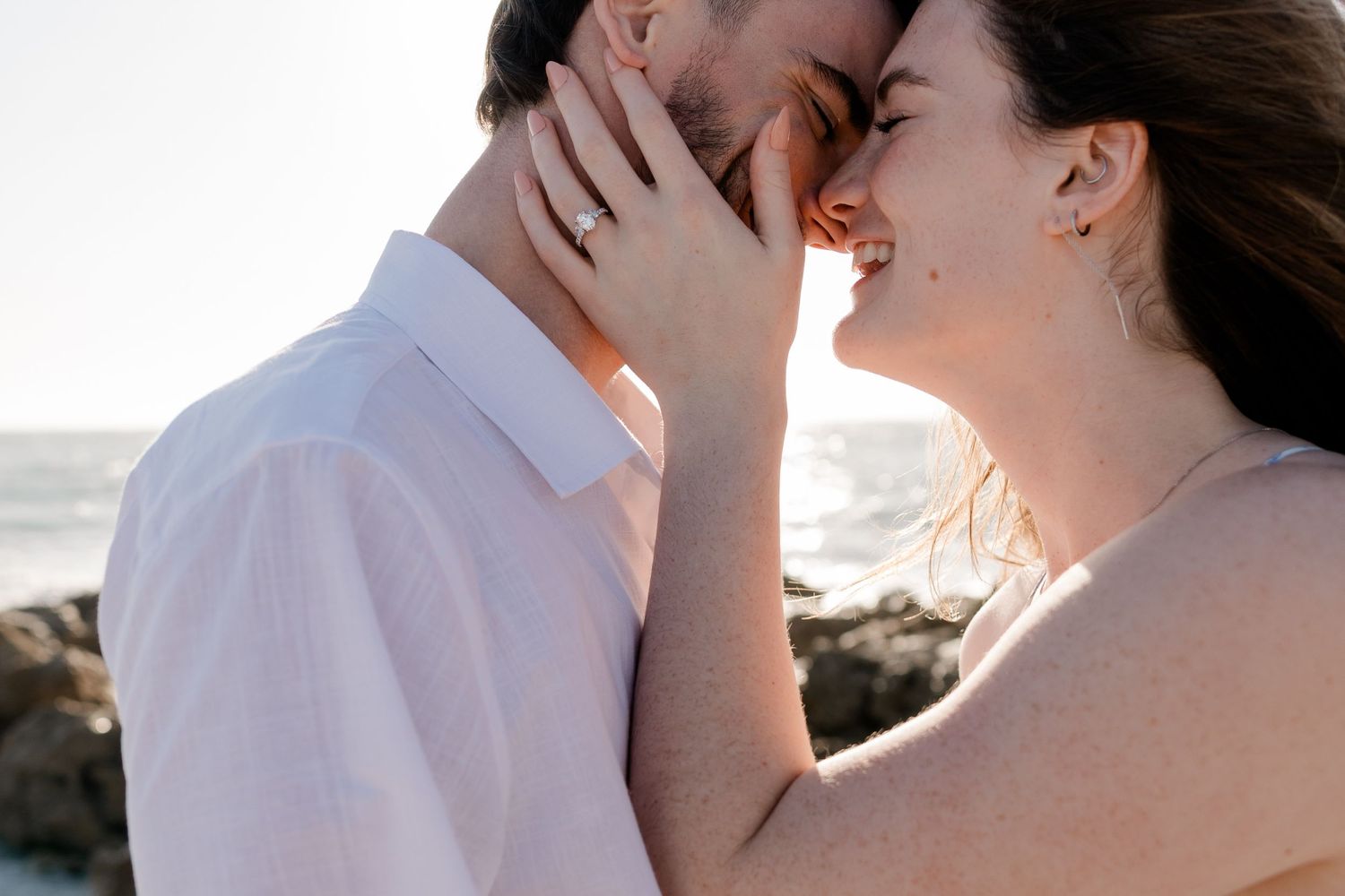 A romantic candid moment between a couple embracing on a rocky beach at sunset.