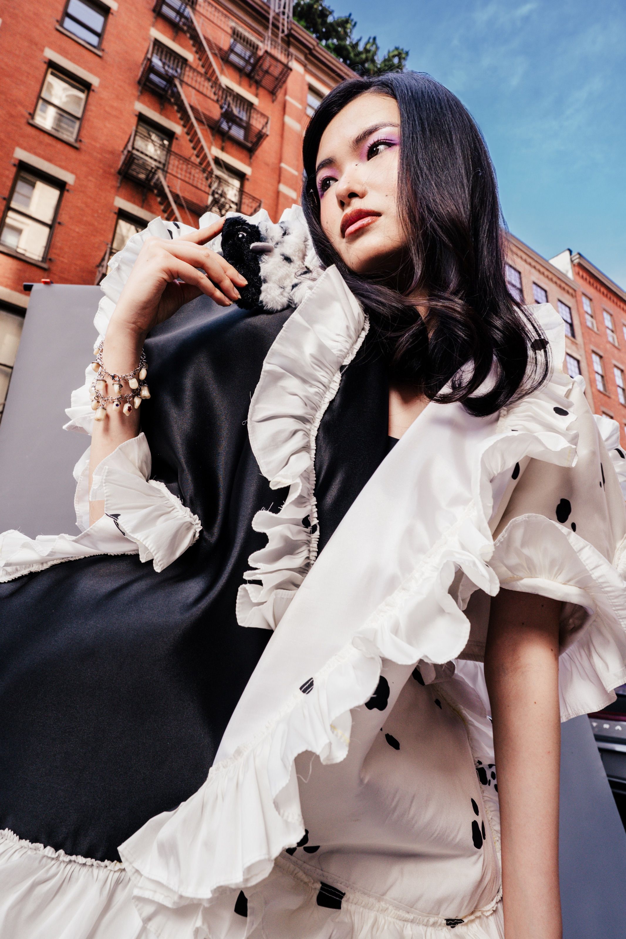 Asian woman in black and white ruffled dress poses outdoors in New York City urban street setting.