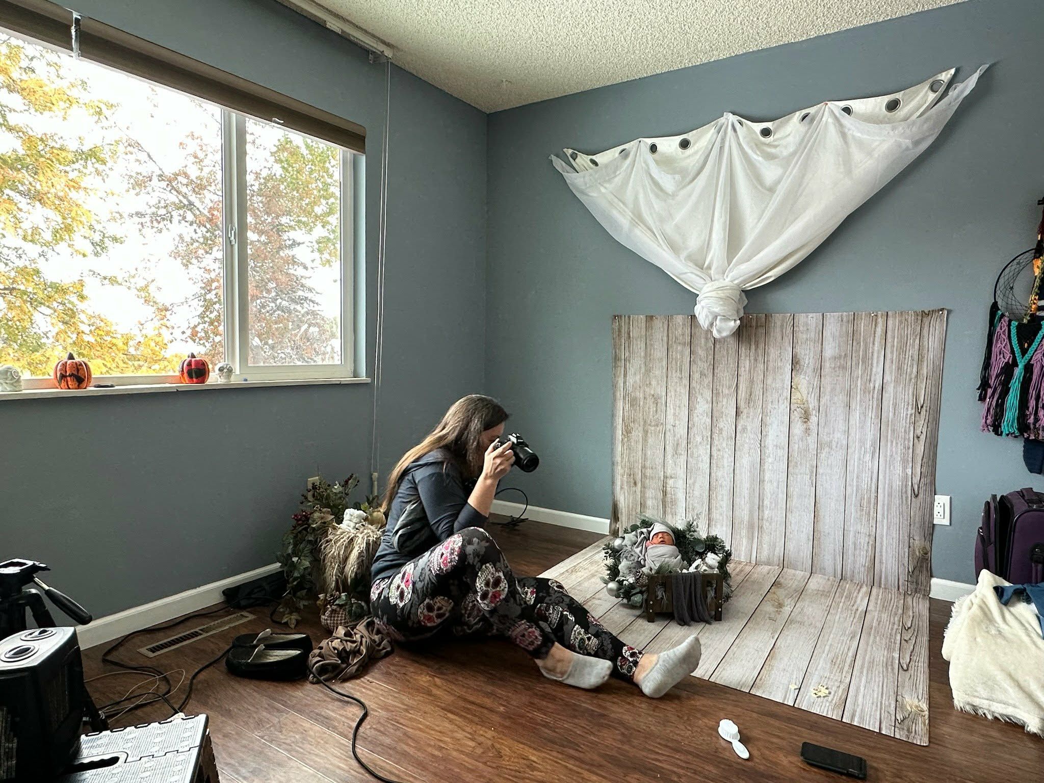 Photographer capturing a newborn baby on a rustic wood backdrop in a blue home photography studio.