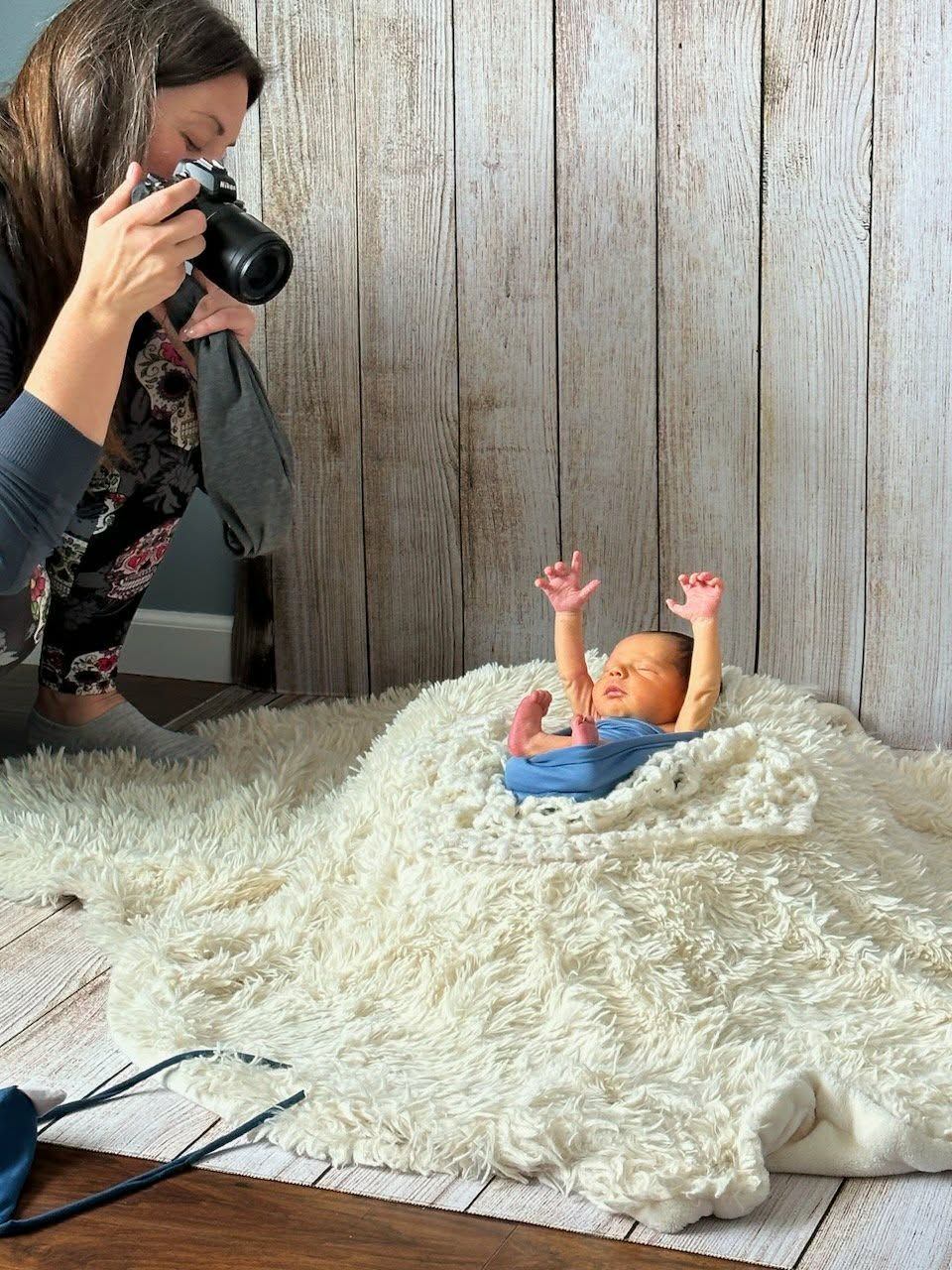 Newborn photographer capturing a baby stretching arms up on fluffy white blanket during professional photo session.