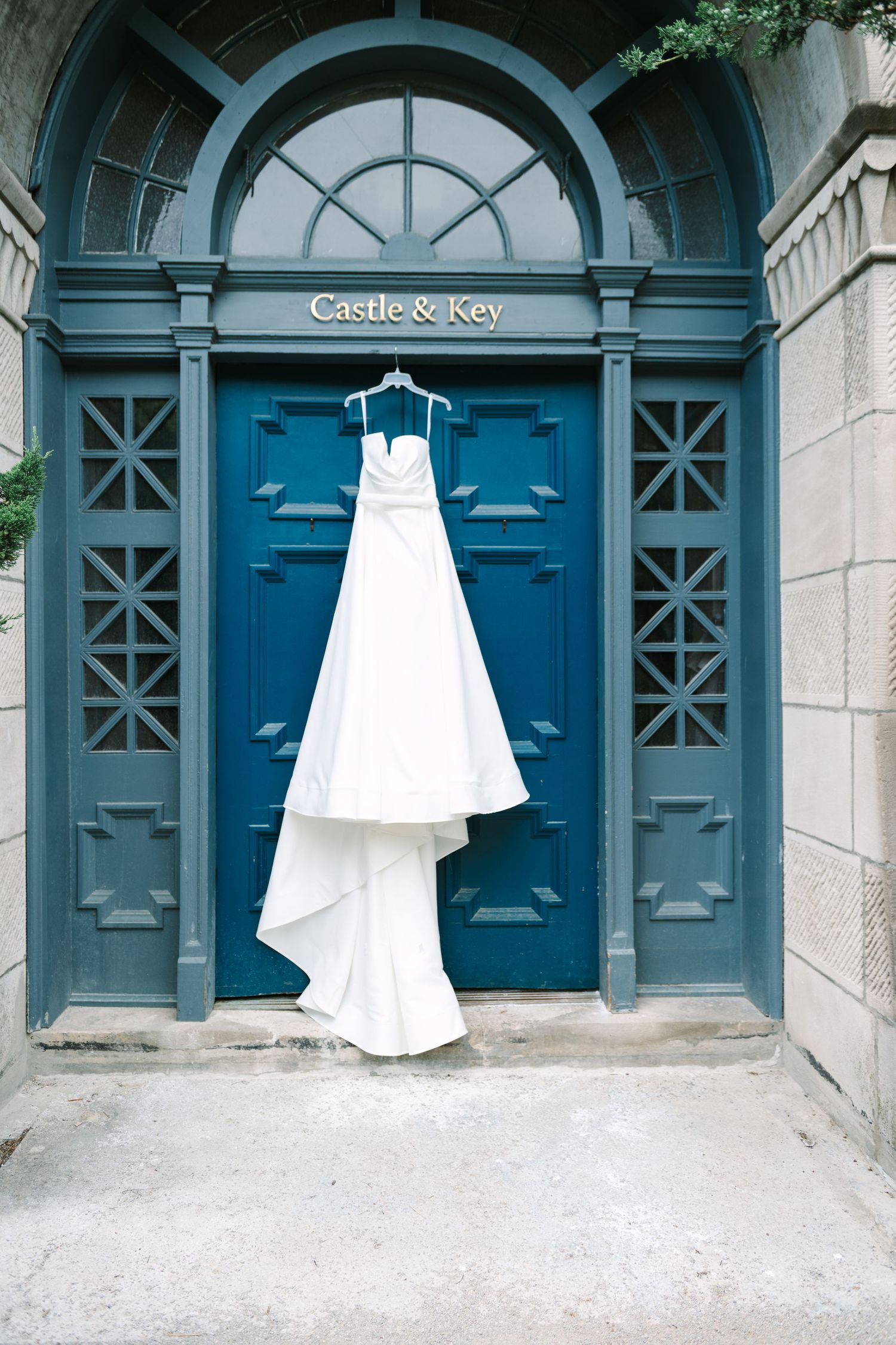 Couple in wedding attire walking along garden path with rustic fence and colorful bouquet.