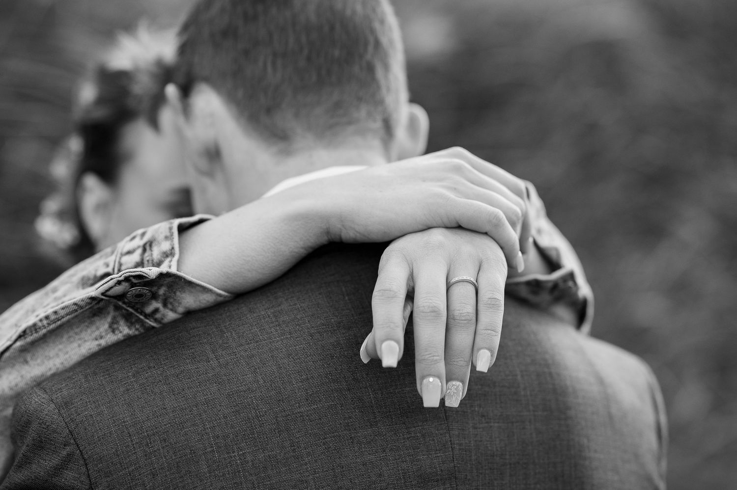 Close-up of hands wearing wedding rings embracing from behind.