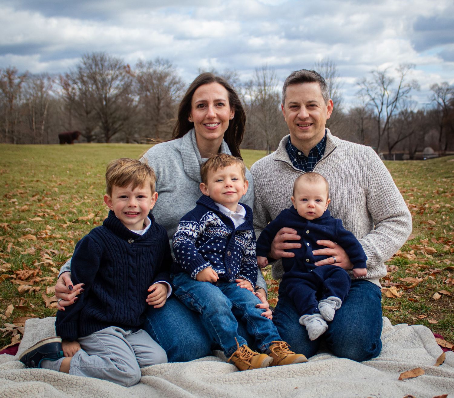 Family outdoor portrait on blanket during fall with cloudy sky background.