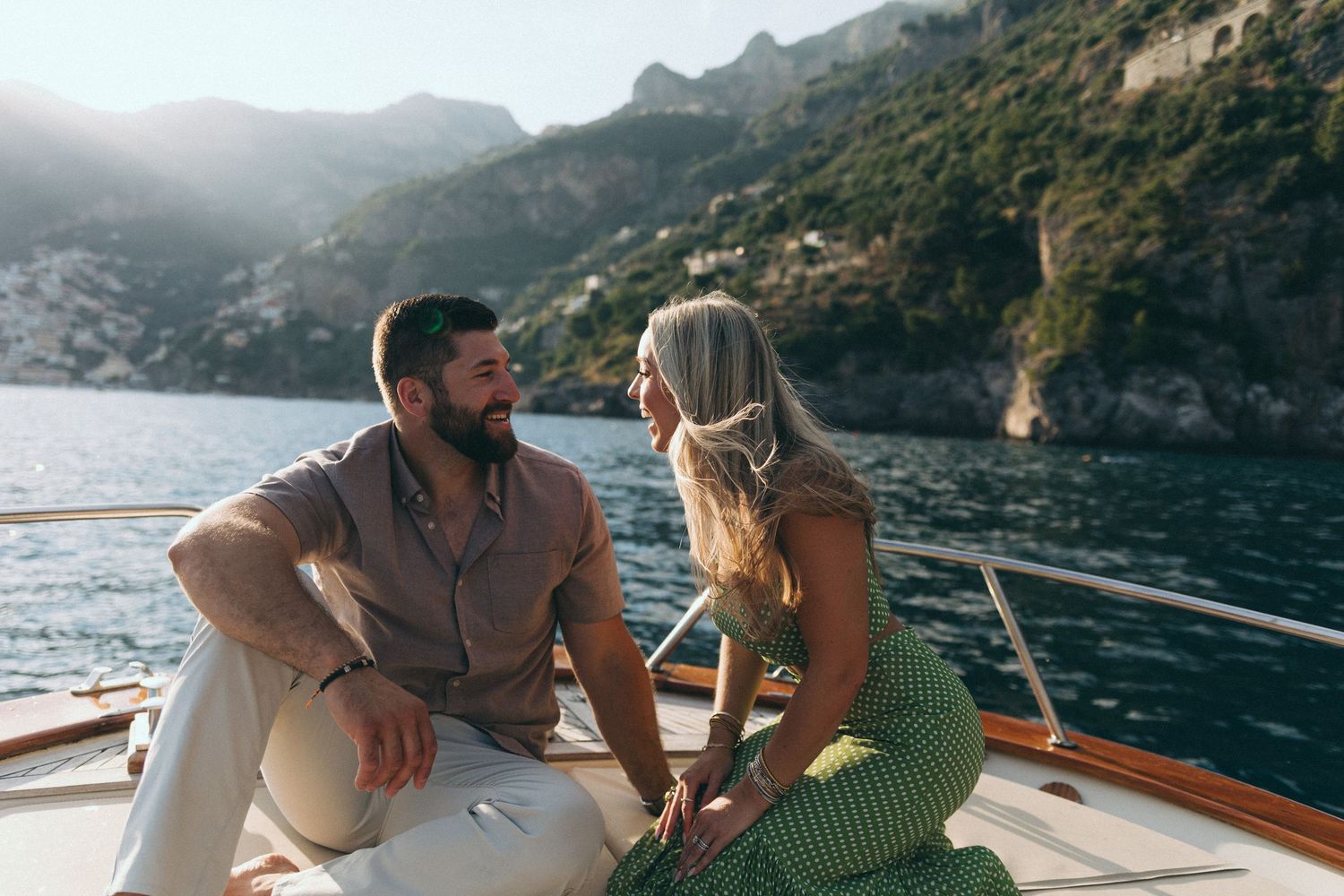 Smiling couple enjoying a romantic boat ride on the Amalfi Coast, sitting together against a scenic mountain backdrop.