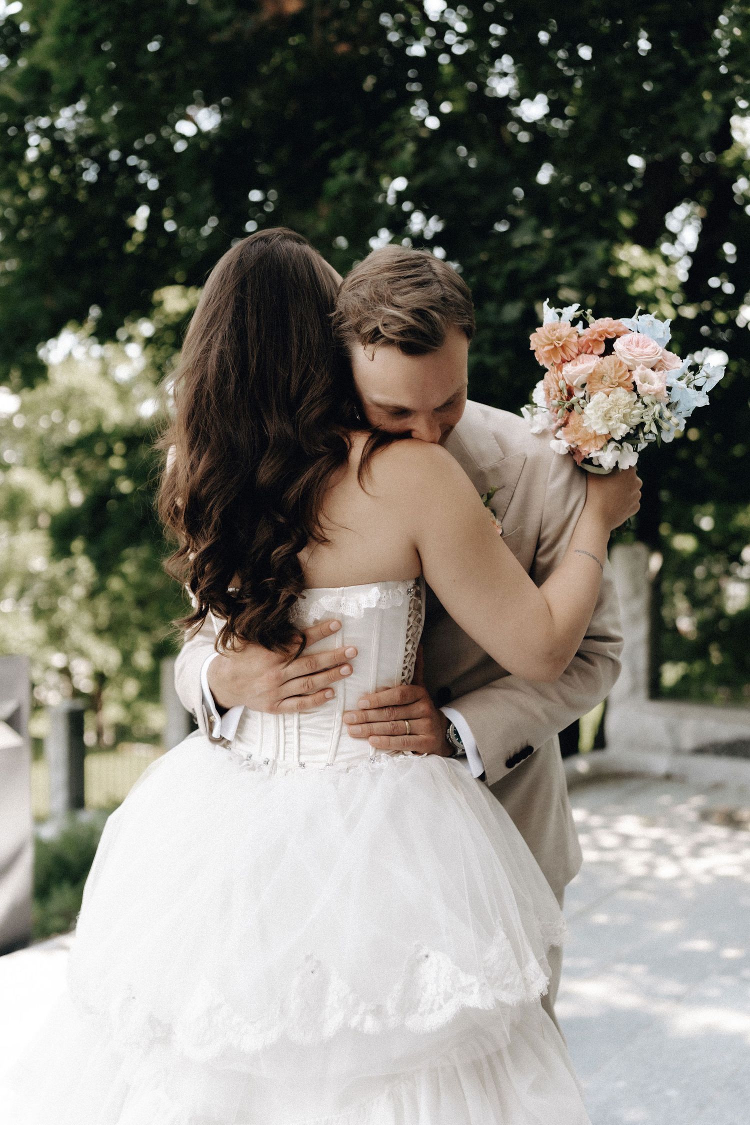 A romantic wedding moment captured outdoors with a beautiful white dress and peach floral bouquet in a garden setting.