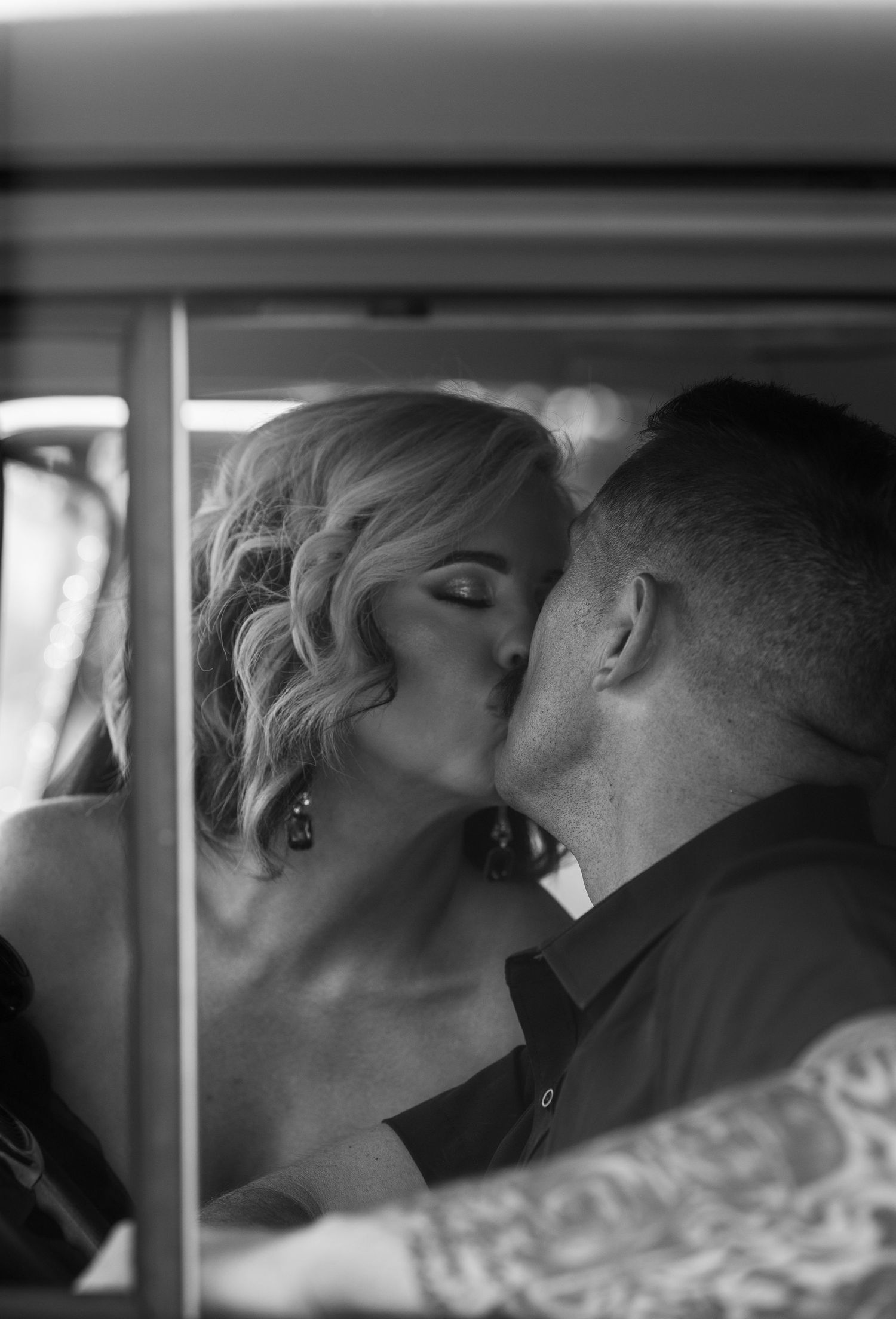 Black and white photo of a couple sharing a passionate kiss inside a vintage vehicle.