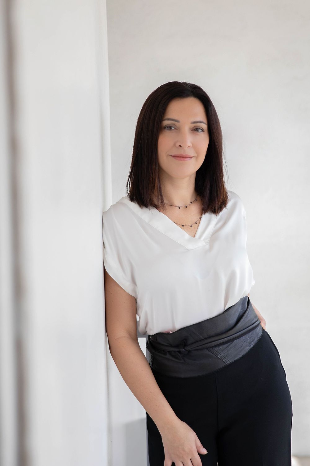 Professional portrait against white wall in business attire with modern minimalist styling.