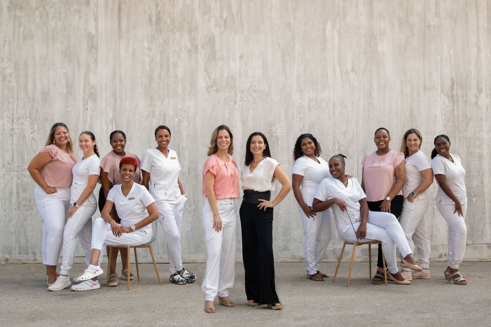 Group portrait of people wearing white and pink outfits against concrete wall.