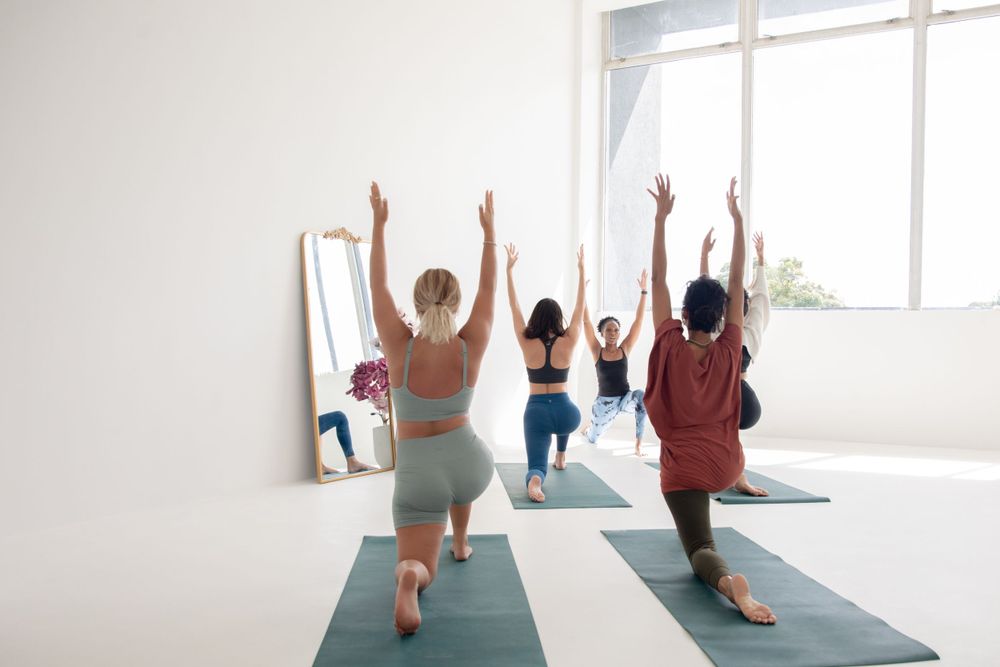A small group wearing workout attire practices yoga poses together in a bright minimalist studio with yoga mats.