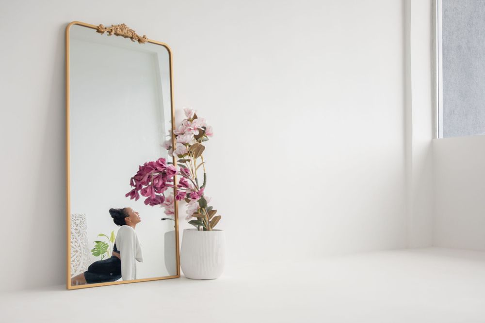 Elegant gold-framed mirror leaning against white wall with pink floral arrangement and decorative objects.