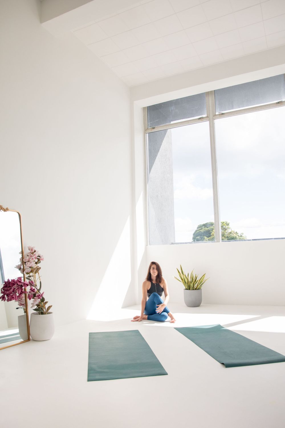 Bright minimalist yoga studio interior with two teal yoga mats on white floor and large window letting in natural light.