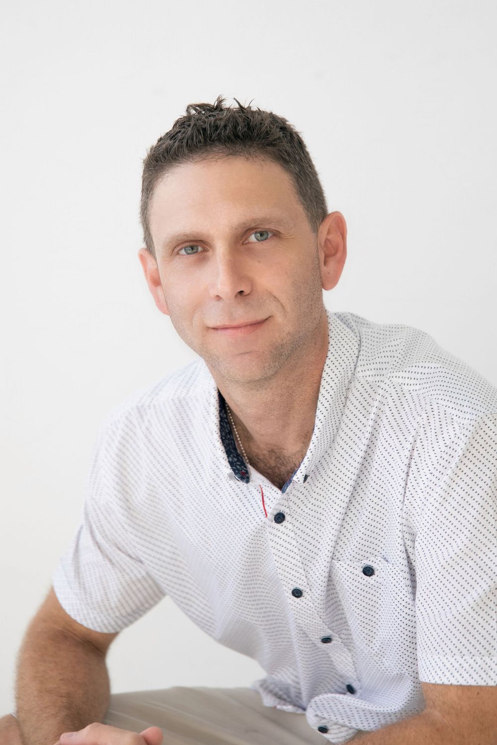 Portrait of someone in a white patterned short-sleeve button-up shirt against a light background.