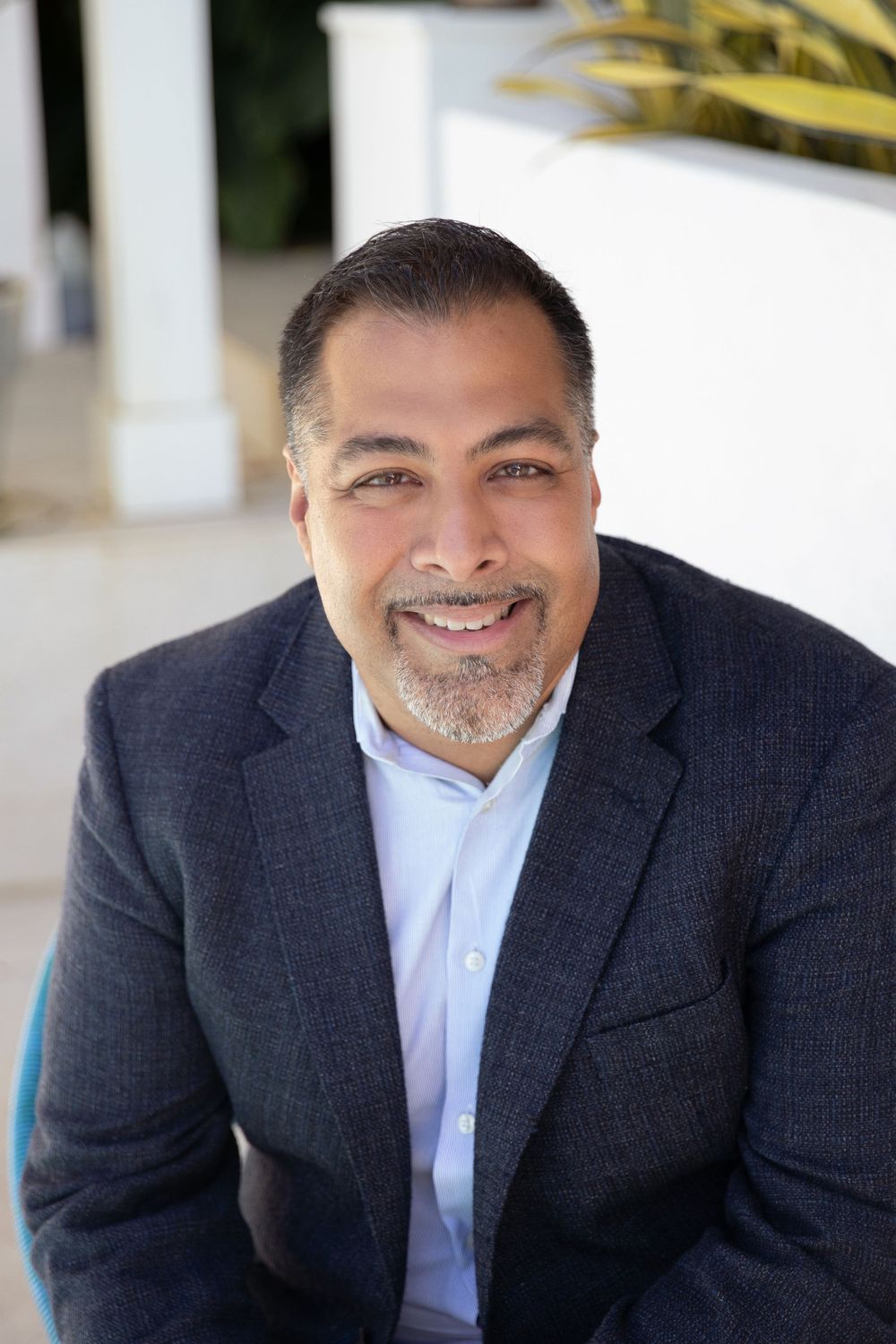 Professional headshot against white tropical architecture backdrop.