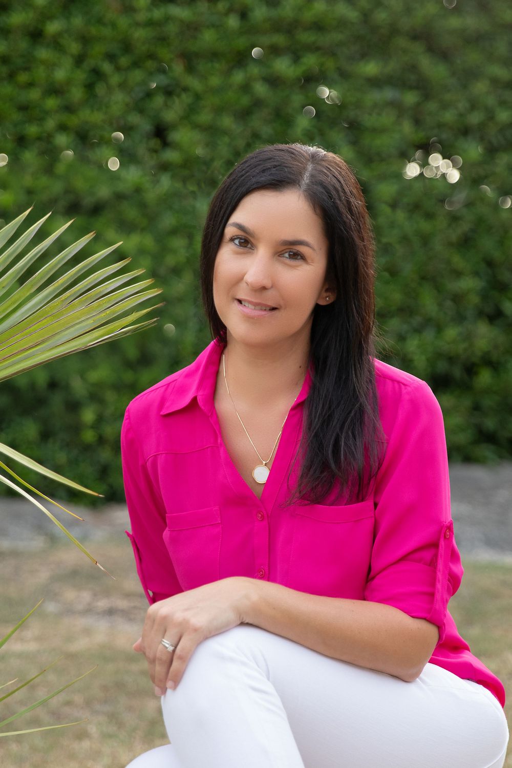 Woman in bright pink blouse holding palm frond while sitting outdoors.