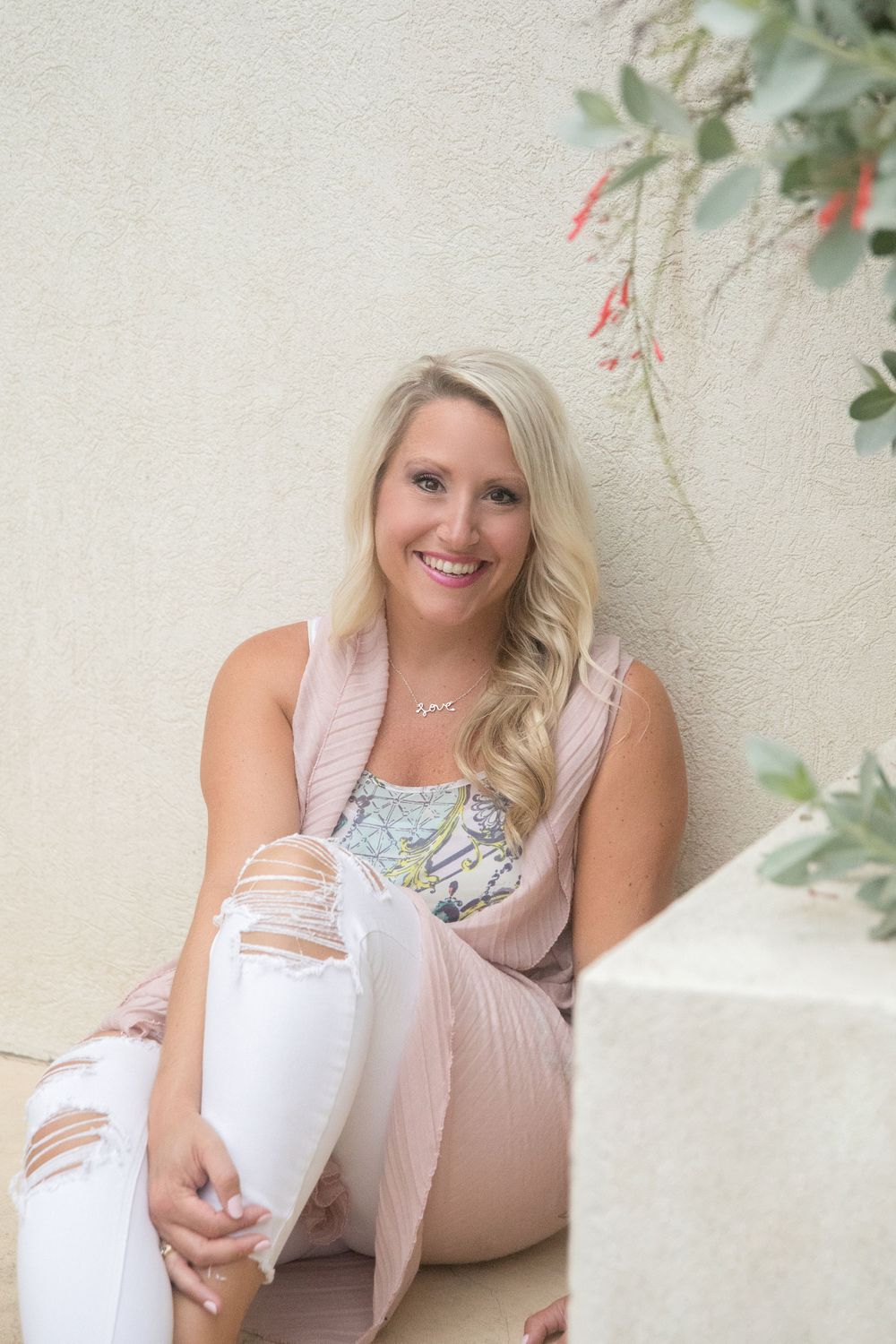 Woman in casual attire sitting on white ledge with decorative plants in background.