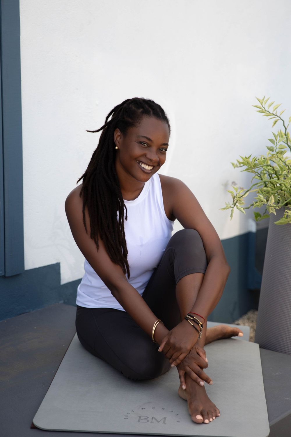 Woman in workout attire sits comfortably on a yoga mat against a white wall.
