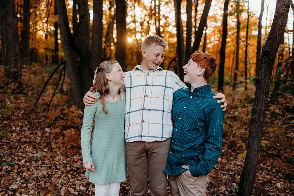 Two brothers and a sister looking at each other laughing and smiling. Leaves are on the ground