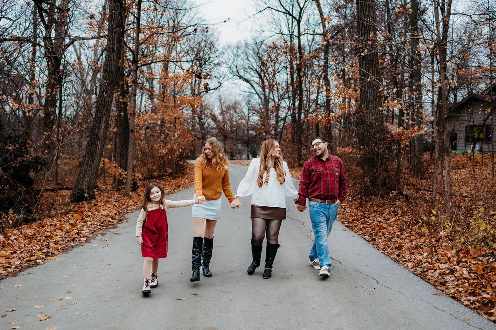 A family of 4 walking together down a path and there leaves on the ground. They are all smiling and laughing.