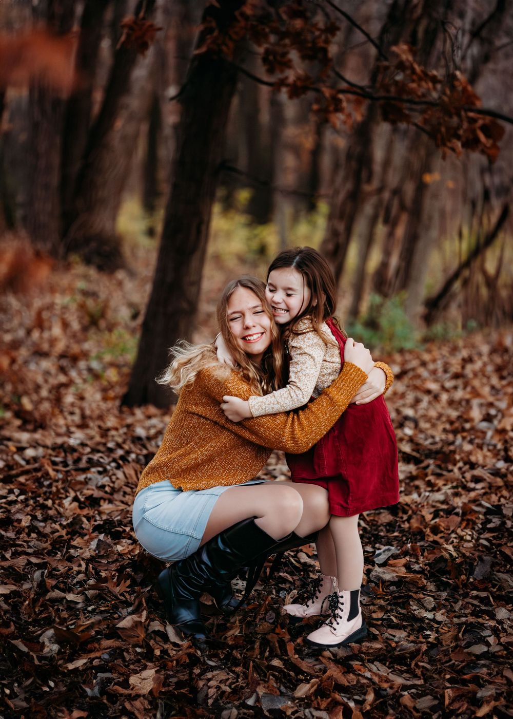 Sisters giving each other a hug and smiling. Leaves are on the ground.