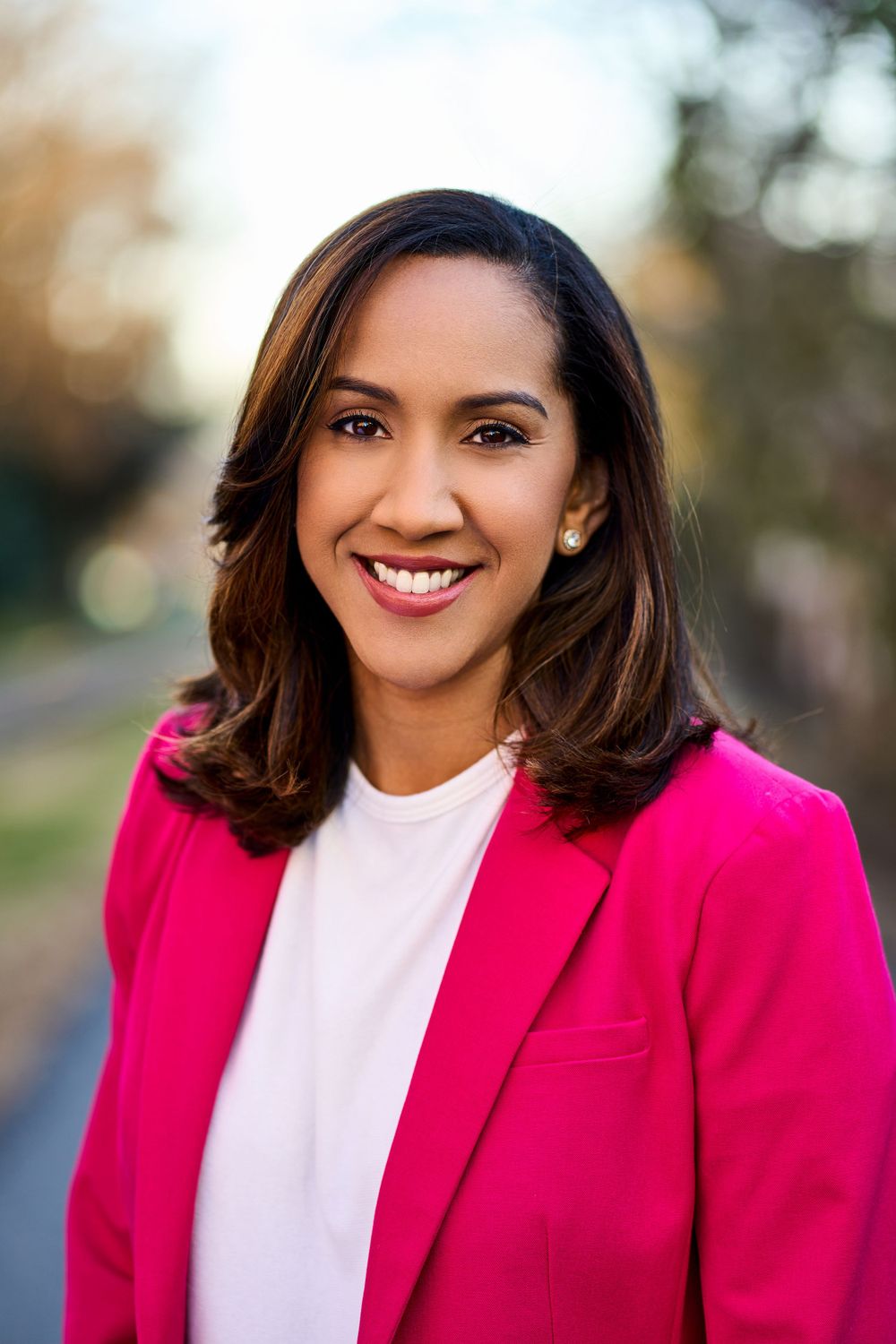 Professional headshot of person in bright pink blazer and white top against blurred background.