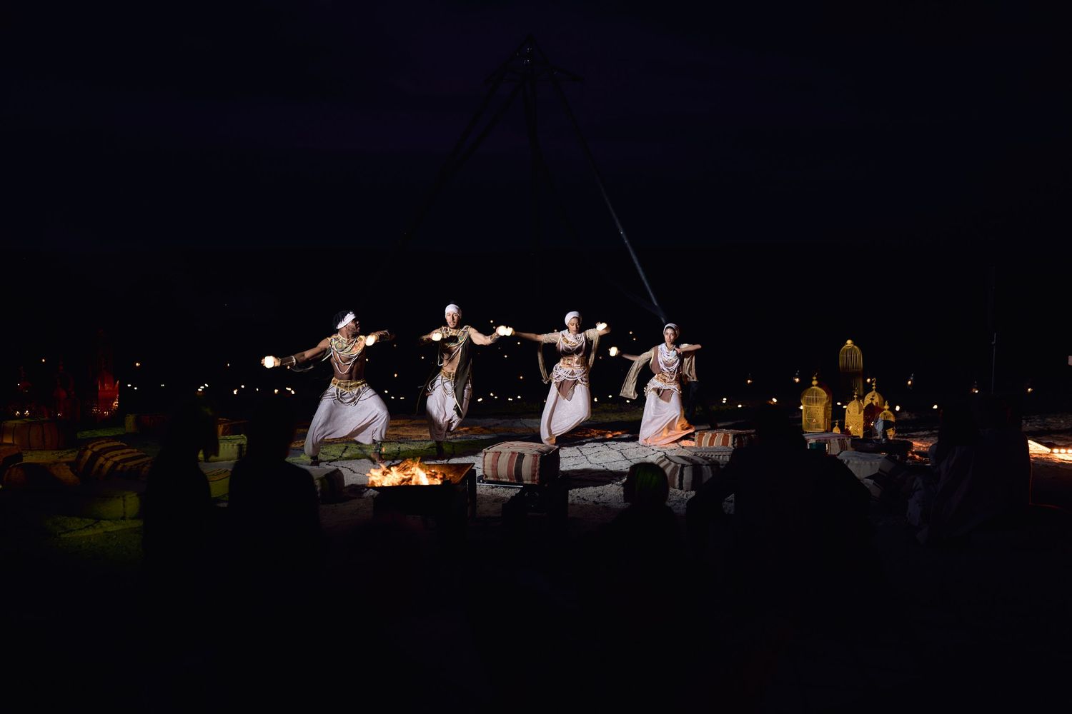 Dancers in white dresses perform gracefully on a dark stage with orchestra musicians visible in the background.